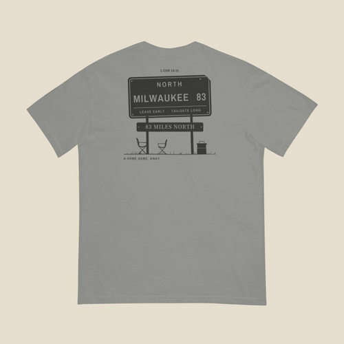 83 Miles North Tailgate Tee, back, Grey: 1 COR 10:31 at the neck over a highway sign reading NORTH, MILWAUKEE 83, two camp chairs and a cooler