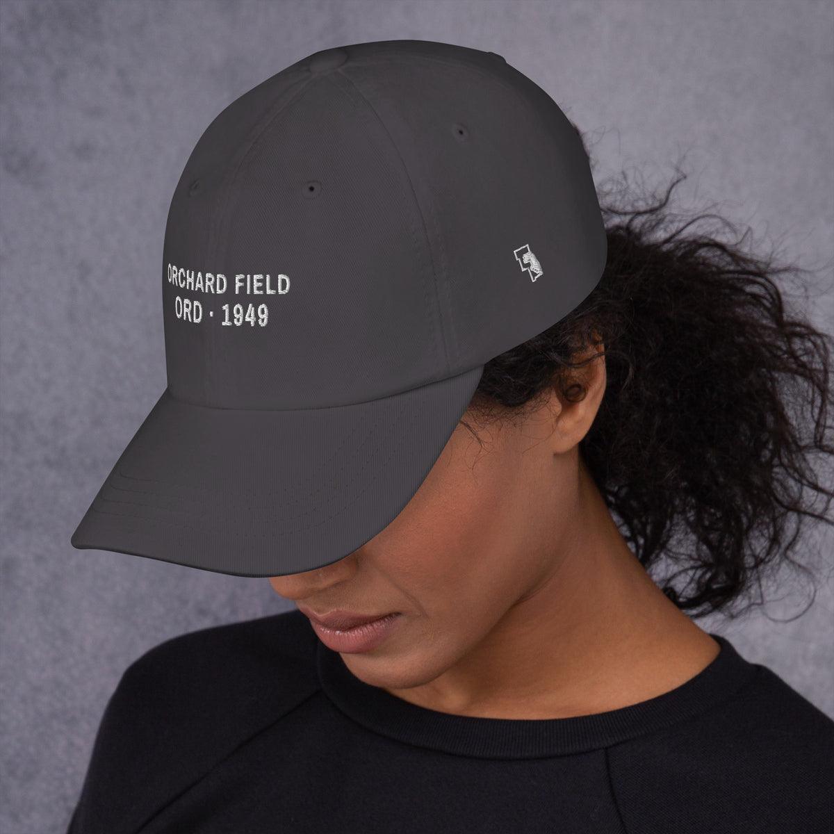 Orchard Field Dad Hat, left side on a model, Dark Grey: ORD lettering and the six counties in white.